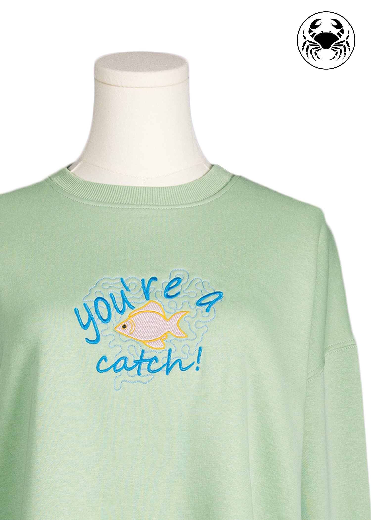 Close-up of pastel green sweatshirt with “you’re a catch” fish embroidery, Canadian apparel